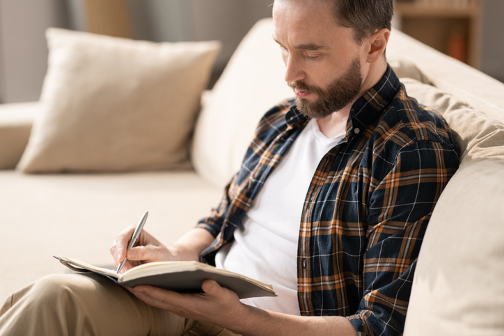 male writing notebook sofa